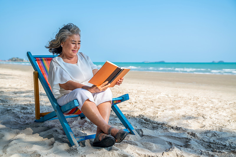 older woman smiling and reading on beach